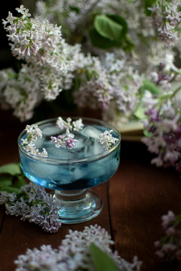 Artistic shot of a blue cocktail adorned with lilac flowers, captured with a dreamy floral backdrop.