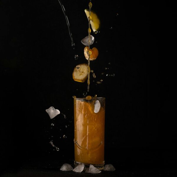 Citrus juice splashes with ice cubes and fruit slices against a black background.