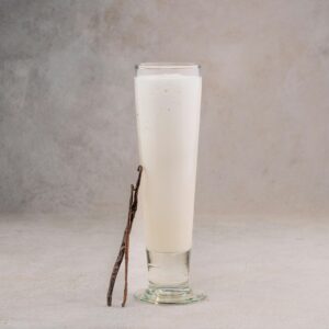 Delicious vanilla-flavored milkshake in a tall glass with a natural beige background, highlighting a fresh vanilla bean garnish.