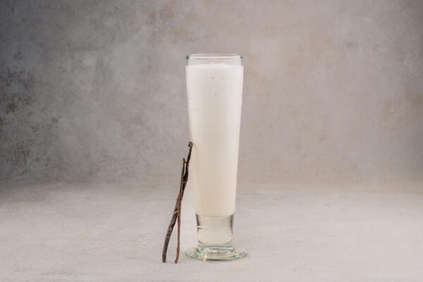 Delicious vanilla-flavored milkshake in a tall glass with a natural beige background, highlighting a fresh vanilla bean garnish.