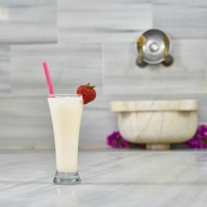 Tall glass of creamy milkshake topped with strawberry, set on a marble surface.