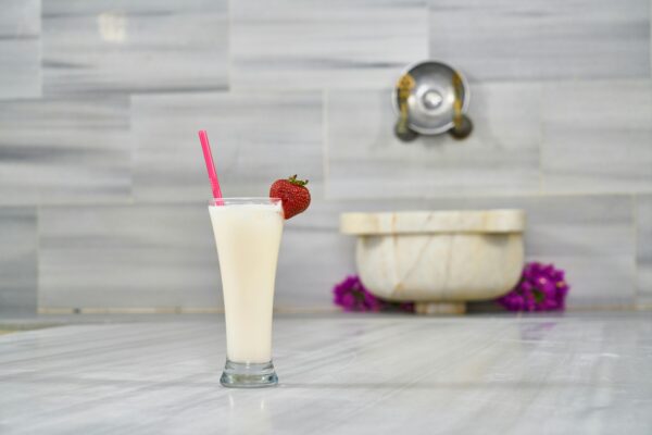 Tall glass of creamy milkshake topped with strawberry, set on a marble surface.