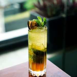 A vibrant mint mojito in a tall glass, garnished with lime and mint leaves, set against a blurred background.