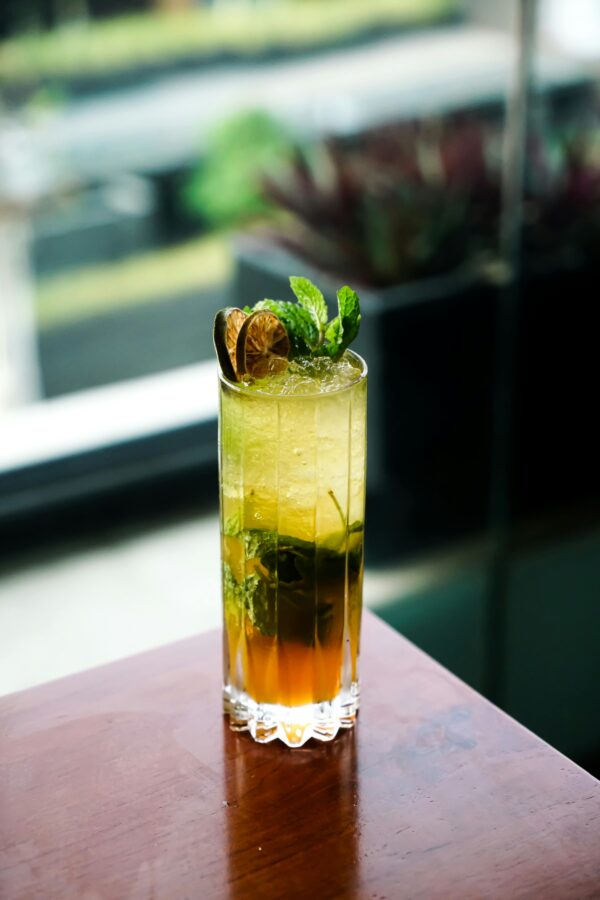 A vibrant mint mojito in a tall glass, garnished with lime and mint leaves, set against a blurred background.