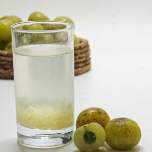 Glass of amla juice beside fresh gooseberries, showcasing a healthy drink choice.