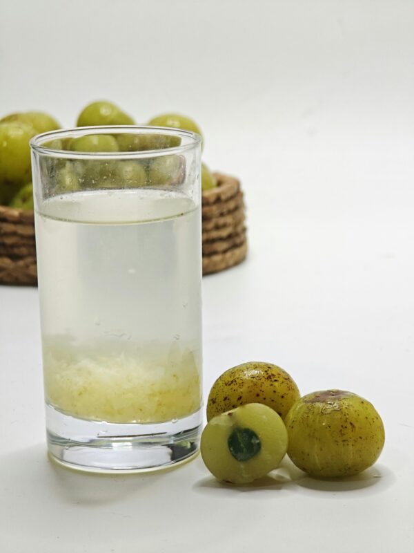 Glass of amla juice beside fresh gooseberries, showcasing a healthy drink choice.