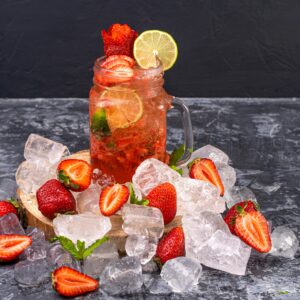 Chilled strawberry lemonade with lime in a mason jar surrounded by ice and fresh strawberries.