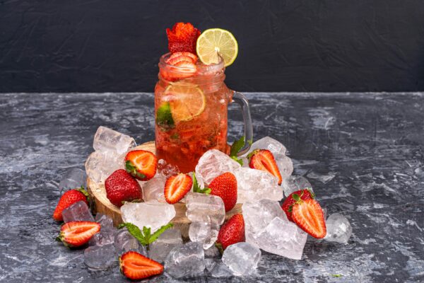 Chilled strawberry lemonade with lime in a mason jar surrounded by ice and fresh strawberries.