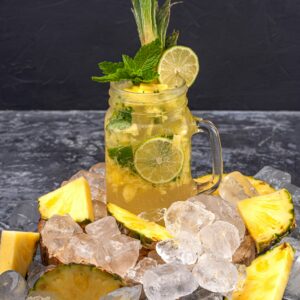 Mason jar with citrus drink and pineapple slices on ice, refreshing and tropical.