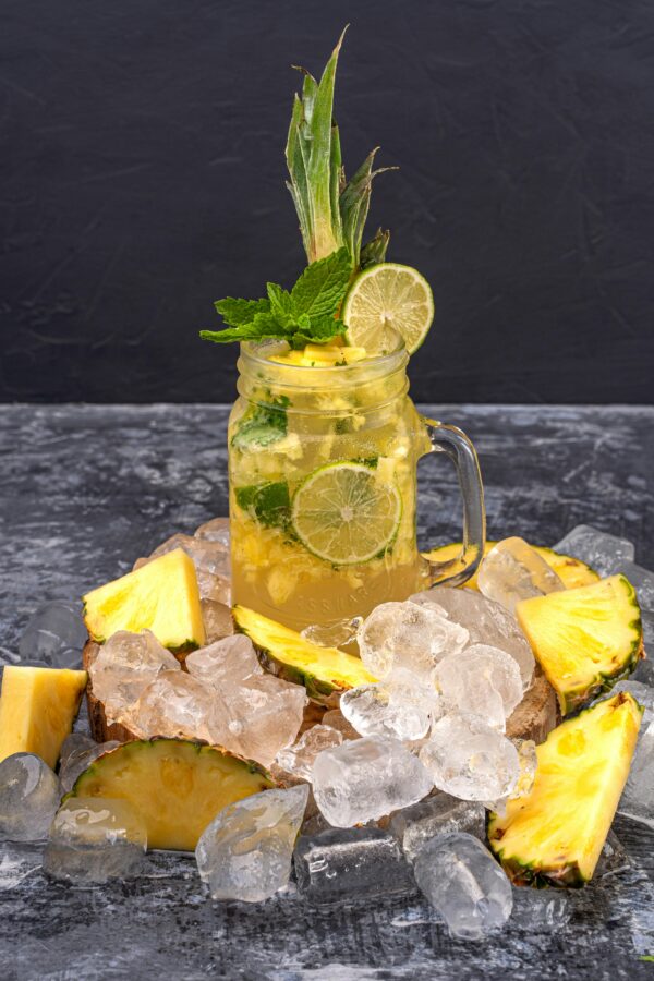 Mason jar with citrus drink and pineapple slices on ice, refreshing and tropical.