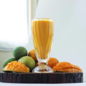Delicious mango smoothie in a glass surrounded by fresh mangoes, perfect for a healthy refreshment.